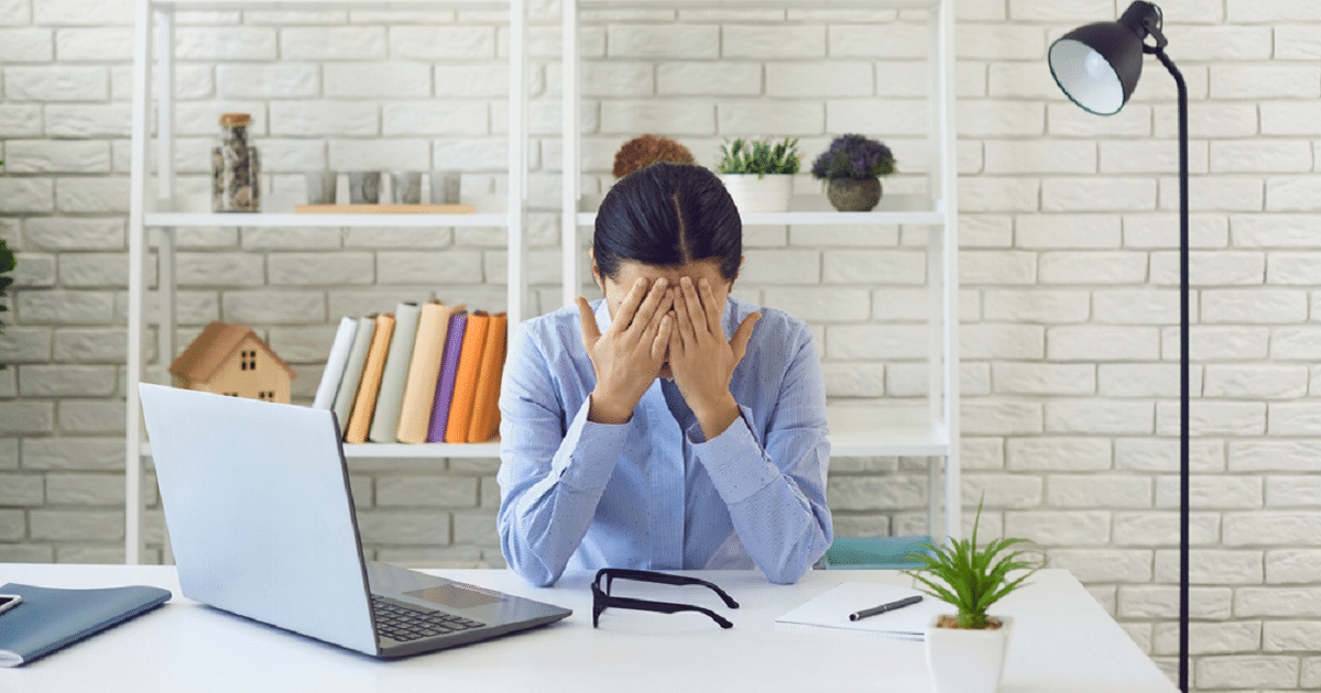 Mujer que sufre los síntomas del estrés laboral con las manos en la cara frente a su ordenador