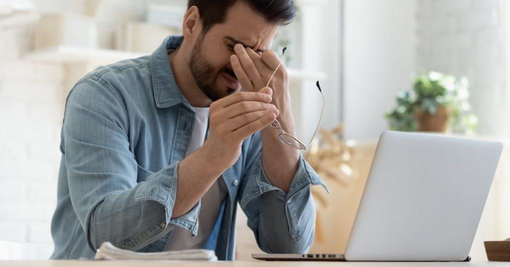 Hombre sentado frente a su ordenador, sufriendo los inconvenientes del teletrabajo