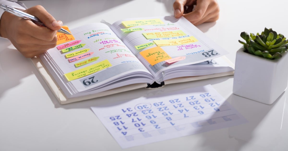Persona trabajadora anotando en una agenda toda sus tareas con post-its y diferentes colores para organizarse y mejorar la productividad