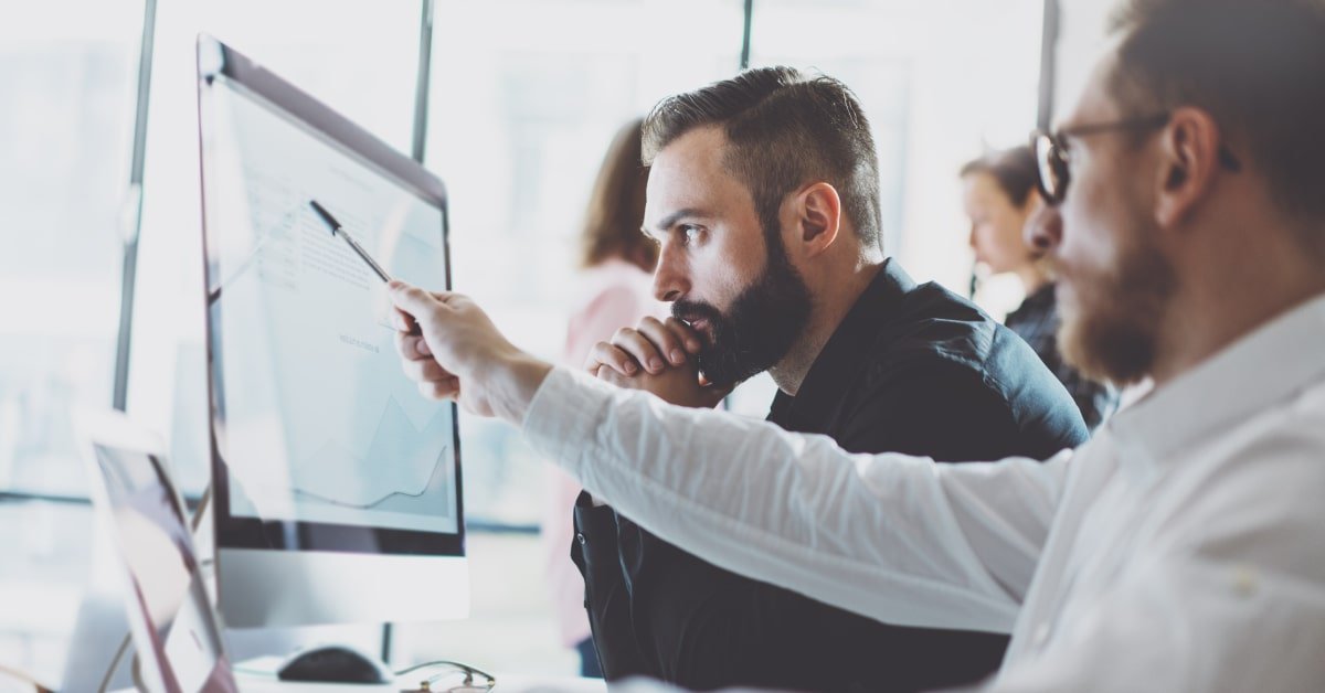 Dos trabajadores realizando una formación online, mientras que uno de ellos señala con un bolígrafo la pantalla del ordenador
